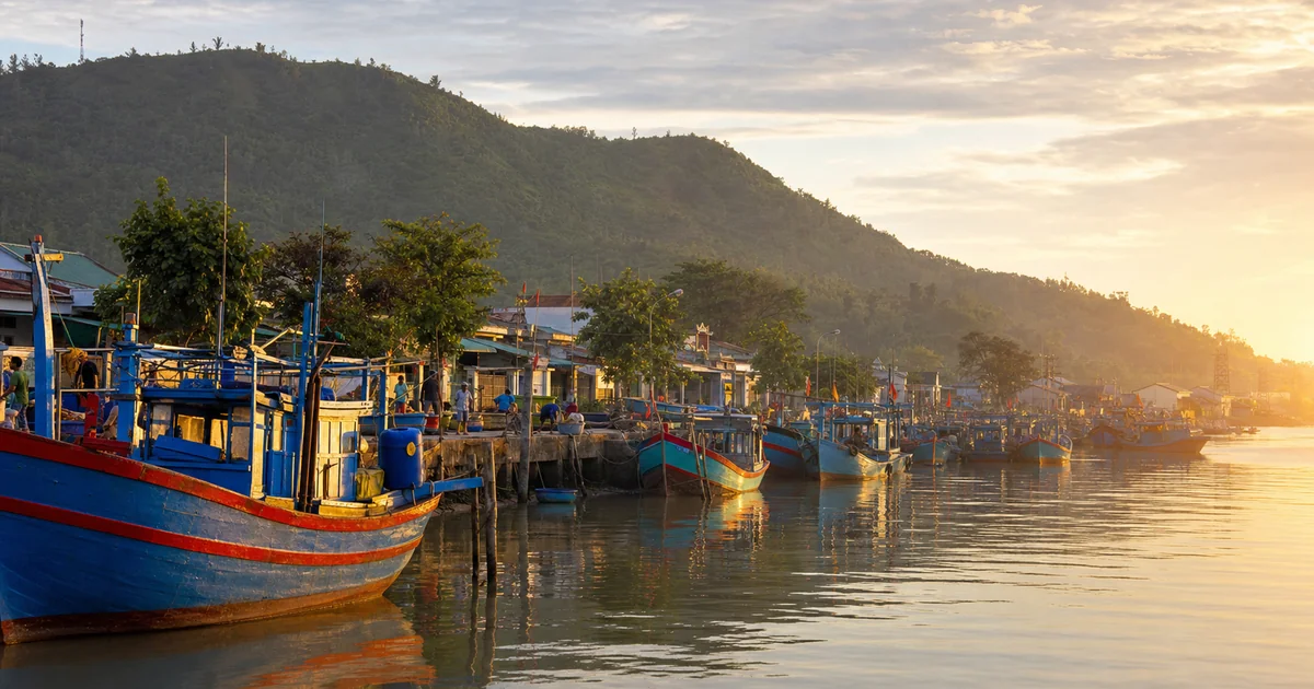 Colourful fishing boats moored along the Duong Dong river at sunrise, with the town's rooftops visible in the soft morning light
