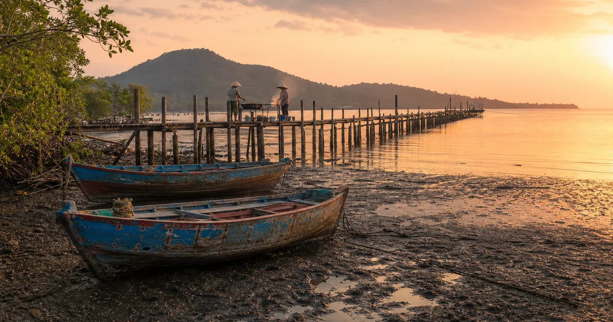 Wooden pier of Ham Ninh fishing village stretching over tidal flats at sunrise with Ham Ninh Mountain in the background, Phu Quoc, Vietnam