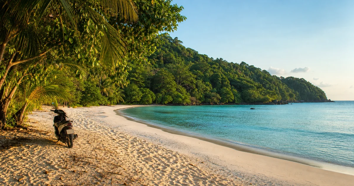 Empty white-sand hidden beach on Phu Quoc fringed by green jungle and calm turquoise water, scooter parked in the background