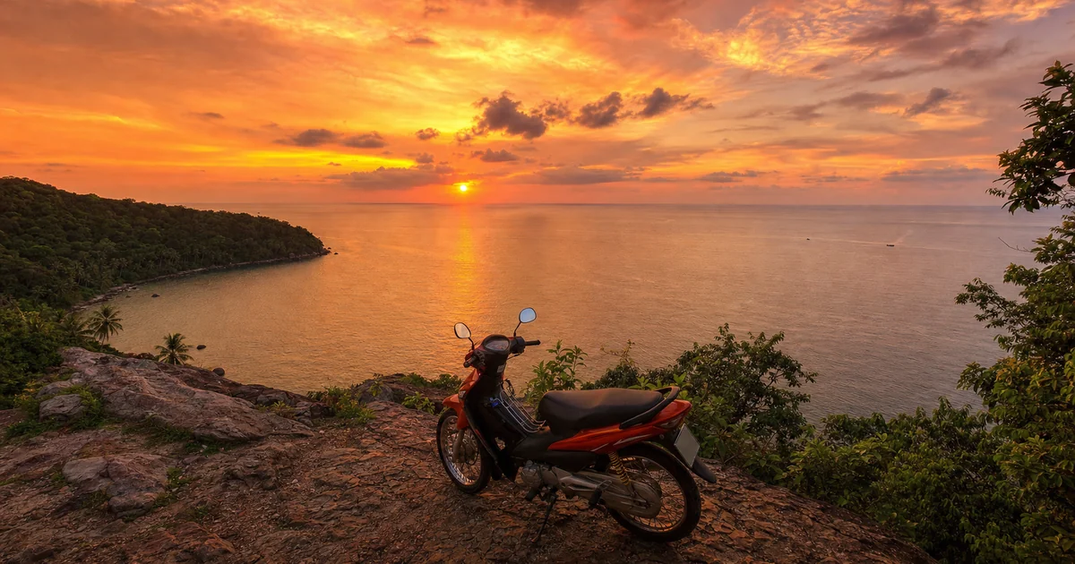 Golden-hour view from a cliff over the Gulf of Thailand near Phu Quoc, motorbike parked in the foreground, sky ablaze with orange and pink hues
