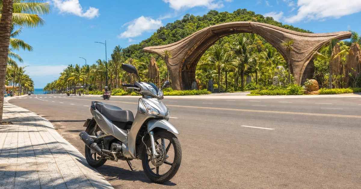 Motorbike parked near the entrance of VinWonders Phu Quoc with palm-lined resort road and blue Gulf of Thailand in the background